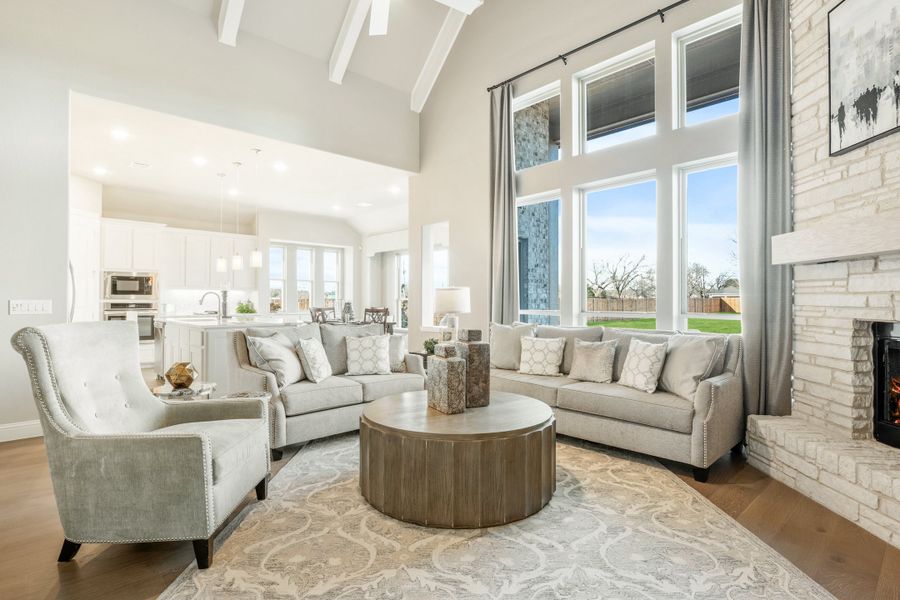 Open-concept living room with vaulted beamed ceiling, stone fireplace, and large windows overlooking backyard Open-concept living room with vaulted beamed ceiling, stone fireplace, and large windows overlooking backyard