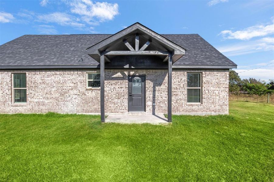Rear view of house with brick siding, a yard, and roof with shingles