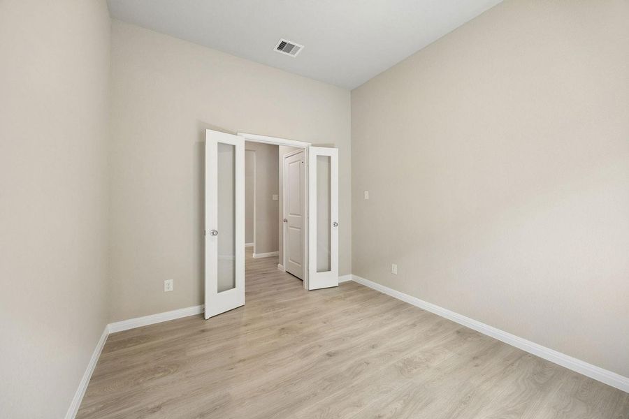 A well-lit room featuring light-toned flooring and elegant double glass doors leading to additional living areas.
