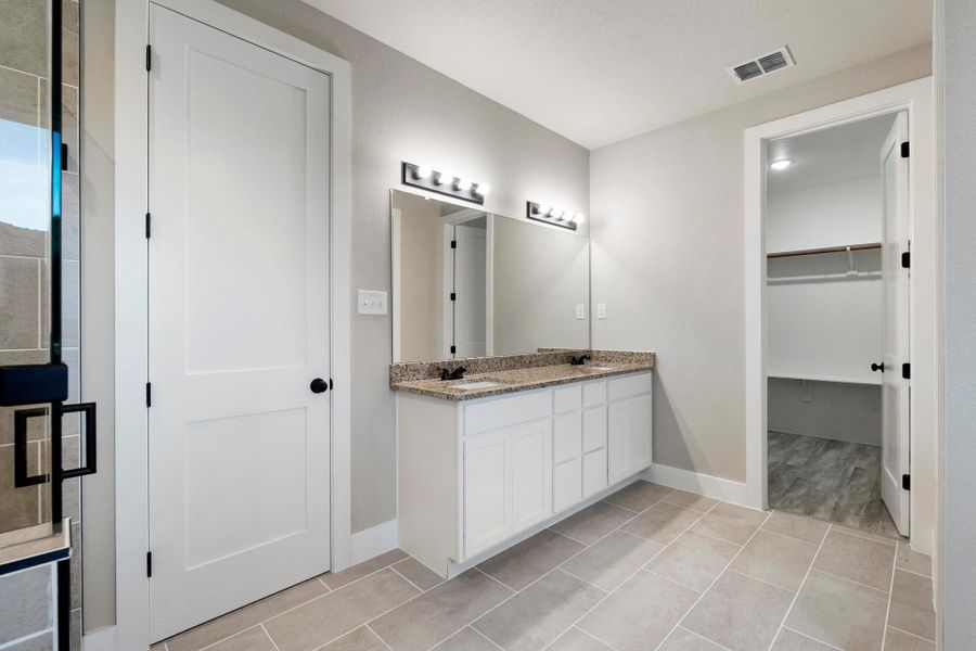 Bathroom with double vanity, a walk in closet, and light tile patterned floors