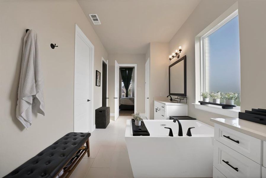 Spacious bathroom featuring a freestanding soaking tub with matte black fixtures, white vanity with stone countertop, and large window Spacious bathroom featuring a freestanding soaking tub with matte black fixtures, white vanity with stone countertop, and large window