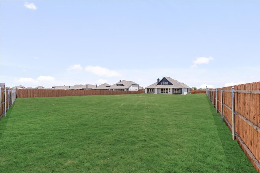 Large backyard with green grass lawn, wood privacy fences on both sides, and home visible in background