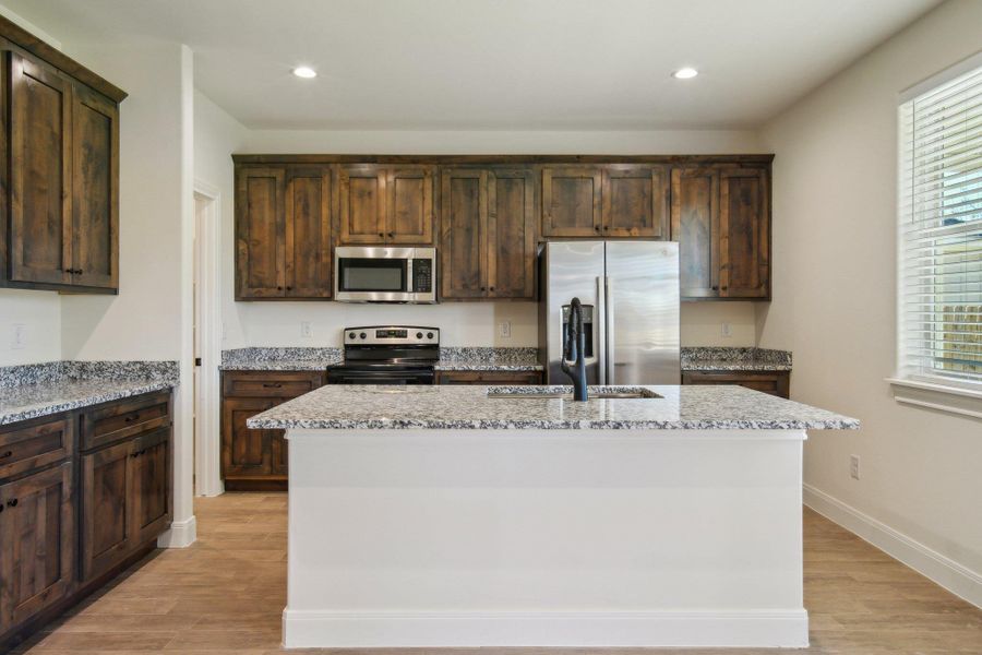 Kitchen with a center island, light wood-type flooring, dark brown cabinetry, and stainless steel appliances Kitchen with a center island, light wood-type flooring, dark brown cabinetry, and stainless steel appliances