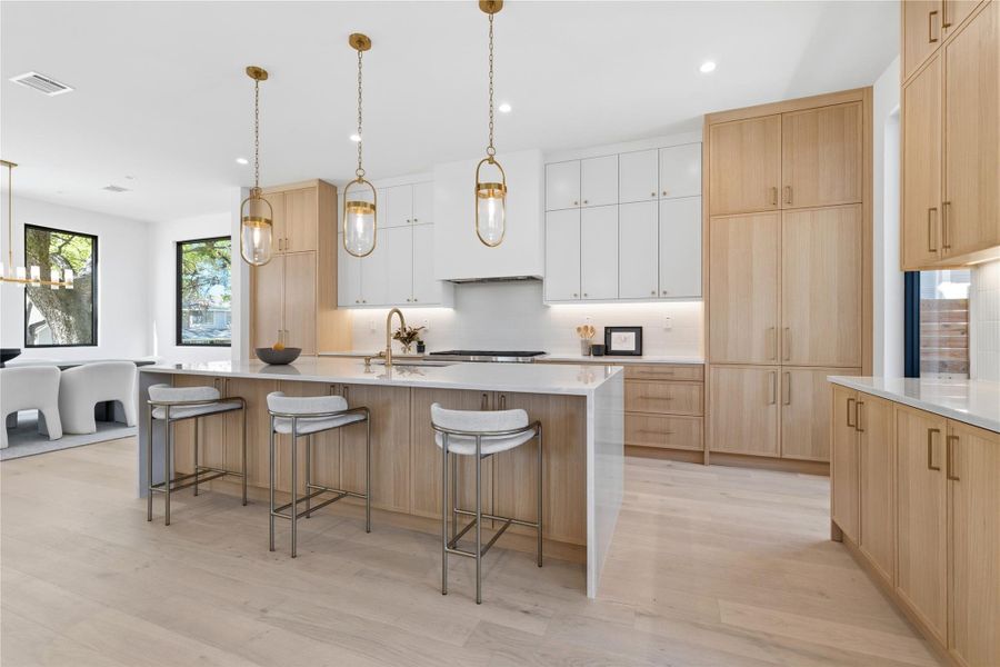 Two tone kitchen with a kitchen bar, two tone cabinets, a large island, light wood-type flooring, and light stone countertops