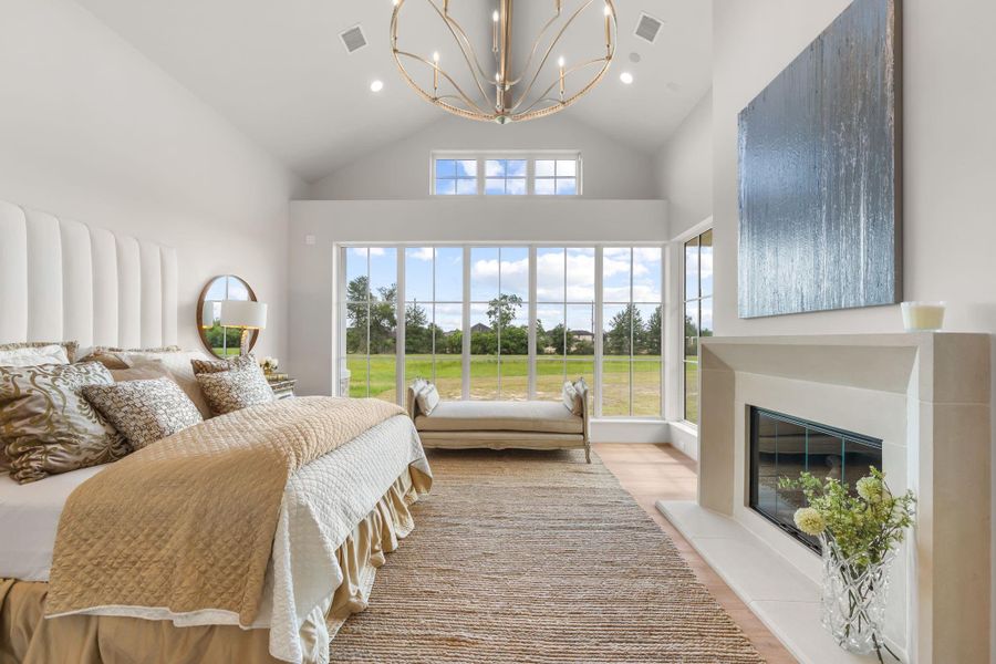 Lavish primary suite with walls of windows, cast stone fireplace and dramatic gold accented chandelier. Lavish primary suite with walls of windows, cast stone fireplace and dramatic gold accented chandelier.