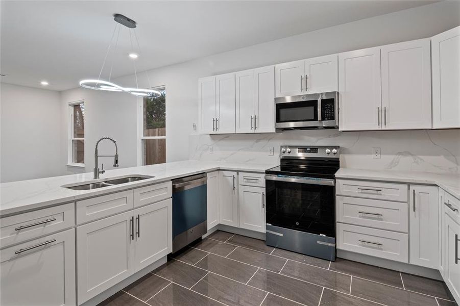 Kitchen featuring sink, hanging light fixtures, stainless steel appliances, decorative backsplash, and white cabinets