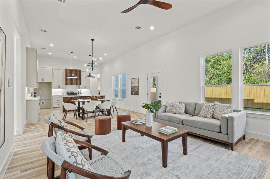 Living area with light wood finished floors, plenty of natural light, recessed lighting, a ceiling fan, and a high ceiling
