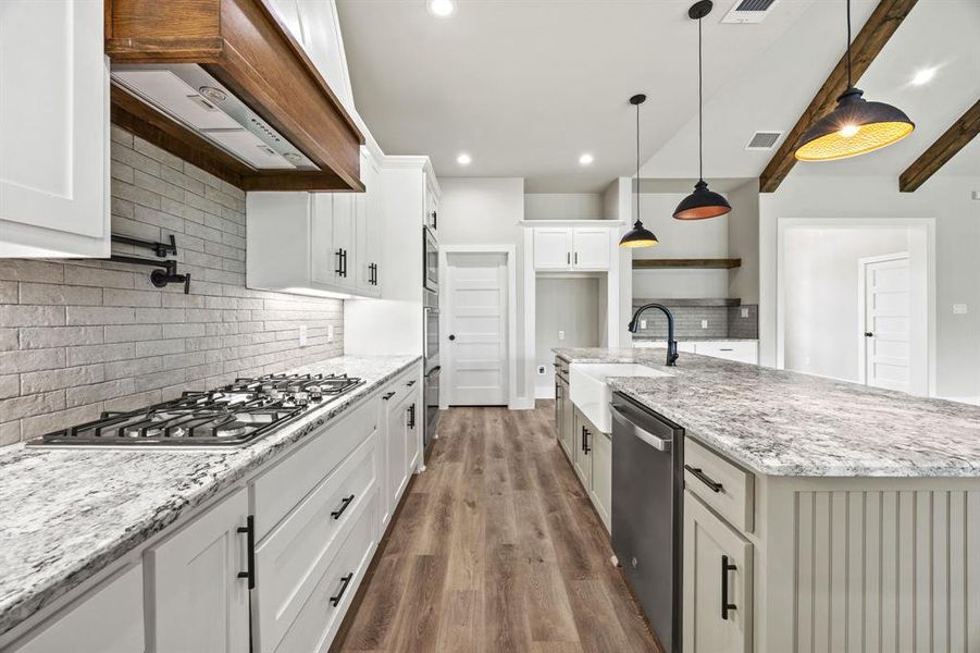 Kitchen featuring light stone counters, beamed ceiling, an island with sink, backsplash, and appliances with stainless steel finishes Kitchen featuring light stone counters, beamed ceiling, an island with sink, backsplash, and appliances with stainless steel finishes