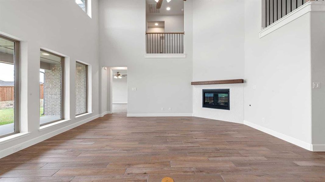 Unfurnished living room with ceiling fan, light wood-type flooring, and a high ceiling