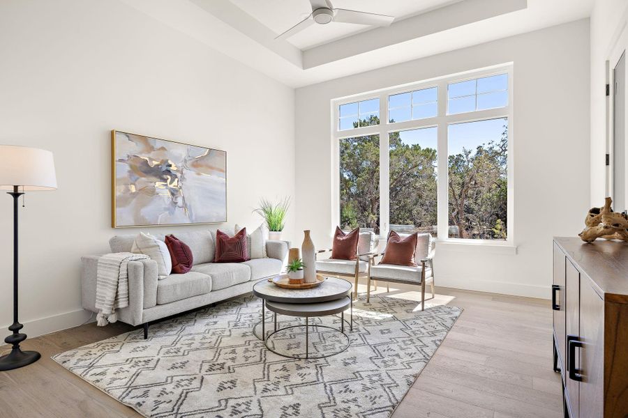 Living area featuring light wood finished floors, a raised ceiling, a ceiling fan, and baseboards