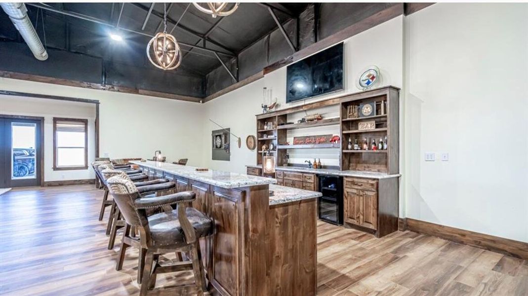 Bar with light wood finished floors, baseboards, wine cooler, and bar Bar with light wood finished floors, baseboards, wine cooler, and bar