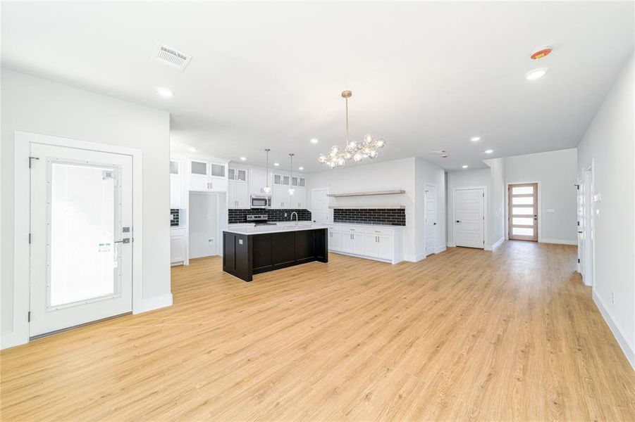 Kitchen featuring a chandelier, glass insert cabinets, open floor plan, white cabinetry, and backsplash Kitchen featuring a chandelier, glass insert cabinets, open floor plan, white cabinetry, and backsplash