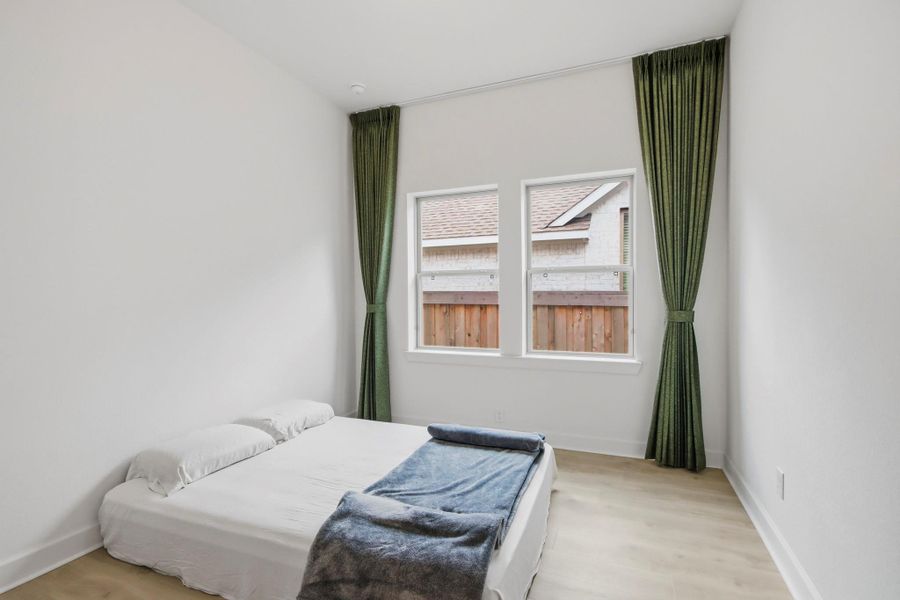 Bright and cozy bedroom featuring tall green drapes, large windows for natural light, and a minimalist design with light wood flooring.