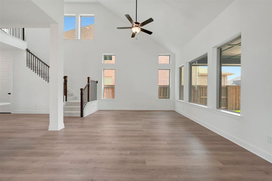 Expansive living area featuring vaulted ceilings with a ceiling fan, wood-finish flooring, and multiple windows