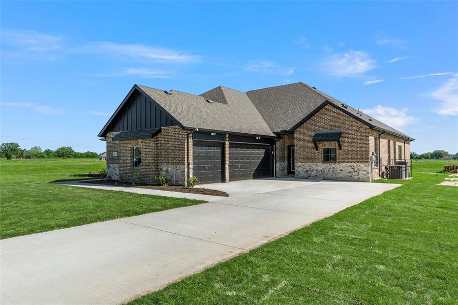 View of front of home with brick siding, board and batten siding, an attached garage, and a front lawn