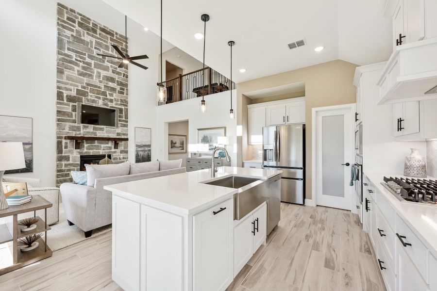 Open-concept kitchen with white island, quartz countertops, and stone fireplace in adjoining living room