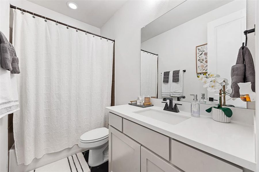 Bathroom featuring vanity, shower / tub combo with curtain, recessed lighting, and toilet