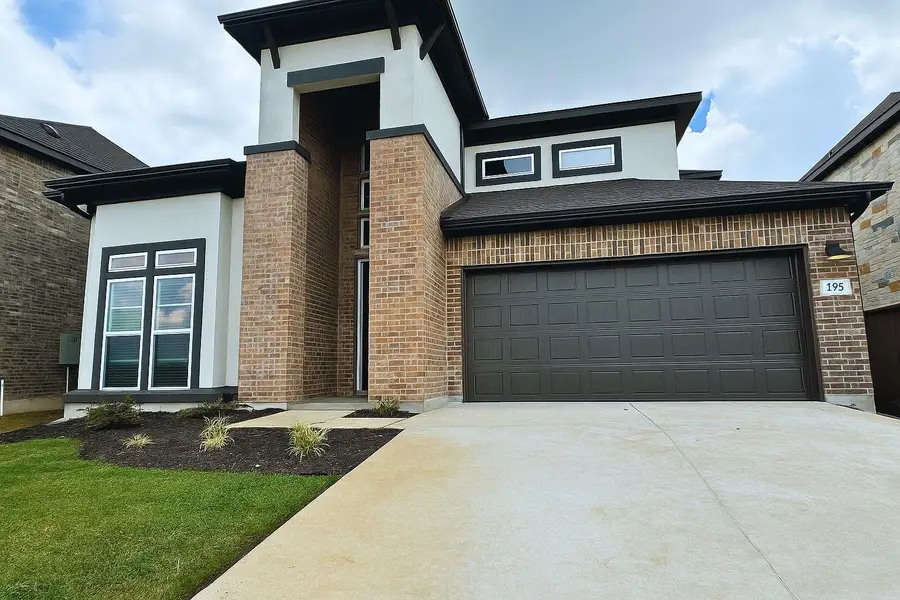 View of front of property featuring brick siding, driveway, a garage, stucco siding, and a front lawn