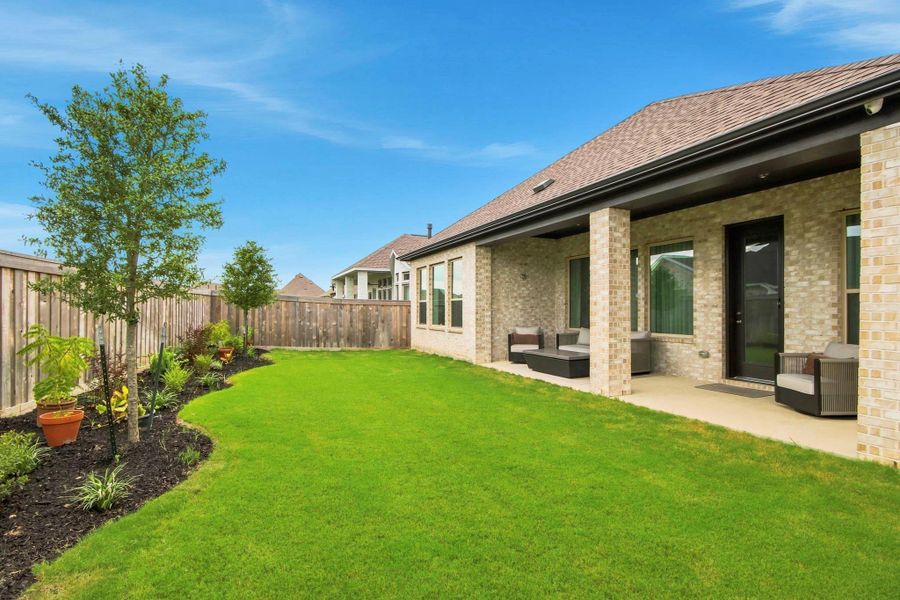 Lush backyard featuring a covered patio, attractive landscaping, and privacy fencing.