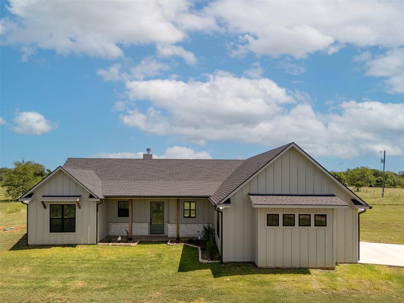 View of front facade with a shingled roof, a porch, a front yard, and a chimney