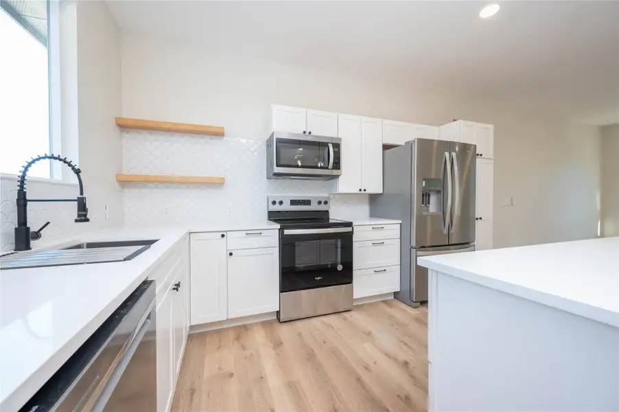 Kitchen featuring stainless steel appliances, tasteful backsplash, light wood finished floors, and white cabinets
