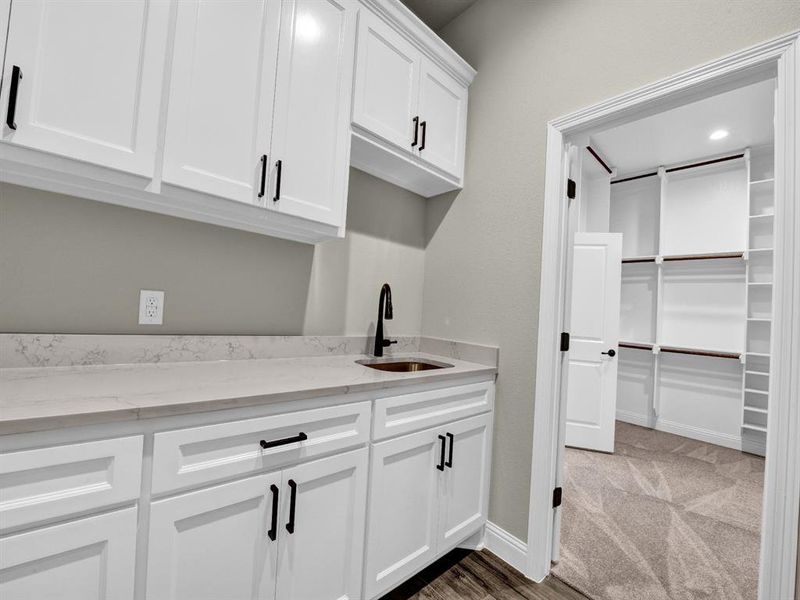 Kitchen with dark colored carpet, sink, white cabinets, and light stone counters