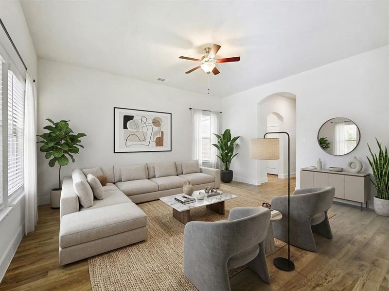 Spacious living area featuring wood-finish flooring, white walls, and a ceiling fan with integrated lighting