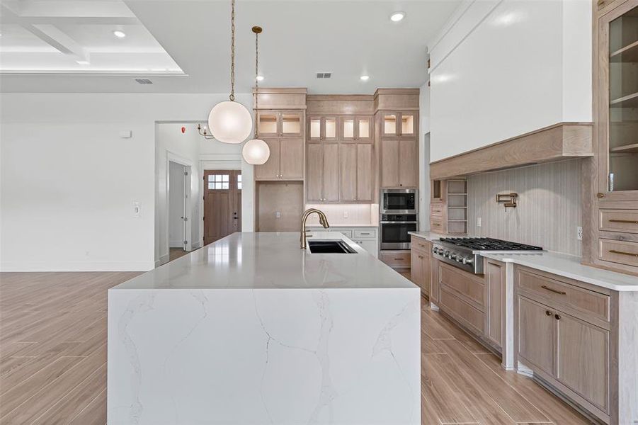 Kitchen with light brown cabinetry, light stone counters, wood tiled floors, pendant lighting, and glass insert cabinets Kitchen with light brown cabinetry, light stone counters, wood tiled floors, pendant lighting, and glass insert cabinets