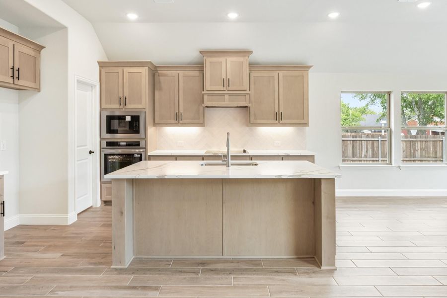 Kitchen with light wood cabinets, marble island, stainless steel appliances, and light wood floors