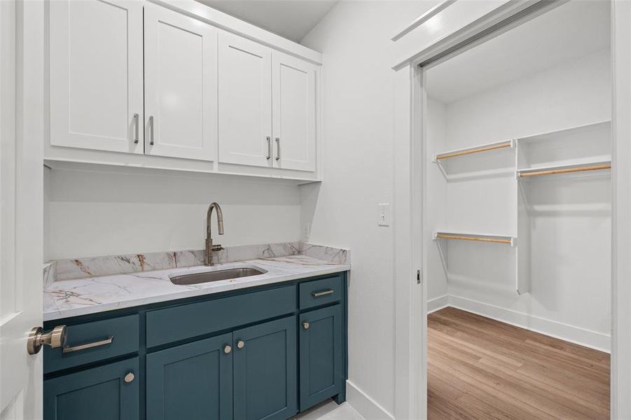 Laundry area featuring a built-in sink with a gooseneck faucet, quartz-finish countertop, white upper cabinetry, and teal lower cabinetry