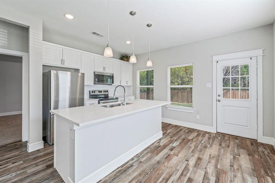 Kitchen with decorative light fixtures, white cabinetry, stainless steel appliances, an island with sink, and recessed lighting Kitchen with decorative light fixtures, white cabinetry, stainless steel appliances, an island with sink, and recessed lighting