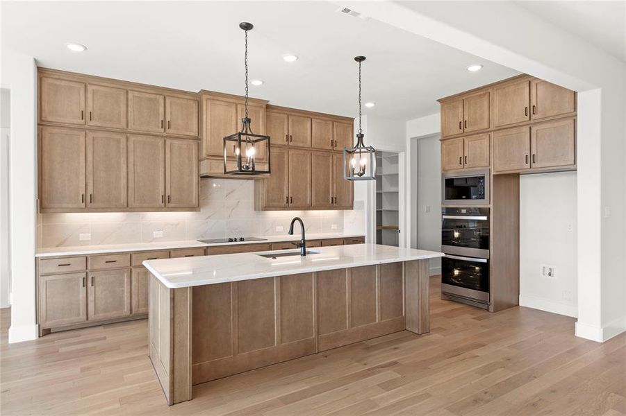 Kitchen featuring pendant lighting, sink, light hardwood / wood-style floors, a center island with sink, and built in microwave