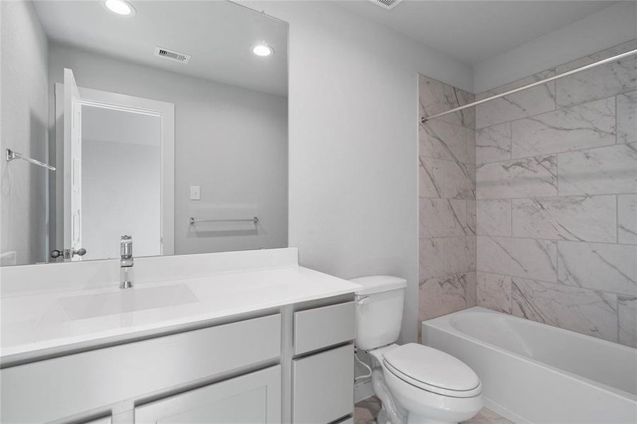 Secondary bath features tile flooring, bath/shower combo with tile surround, stained wood cabinets, beautiful light countertops, mirror, sleek fixtures and modern finishes.