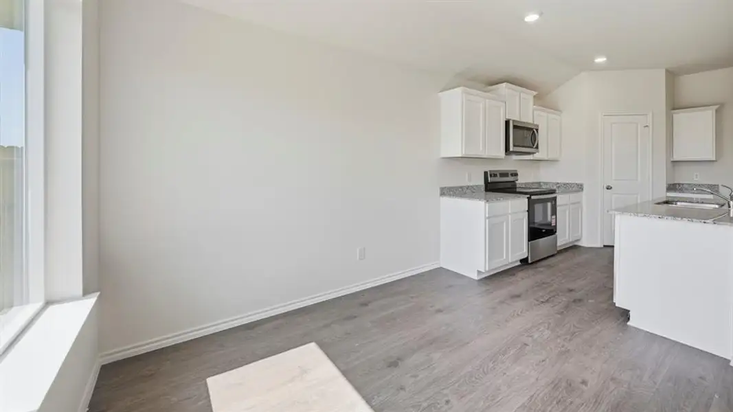 Kitchen with appliances with stainless steel finishes, white cabinetry, light stone counters, light wood-type flooring, and lofted ceiling