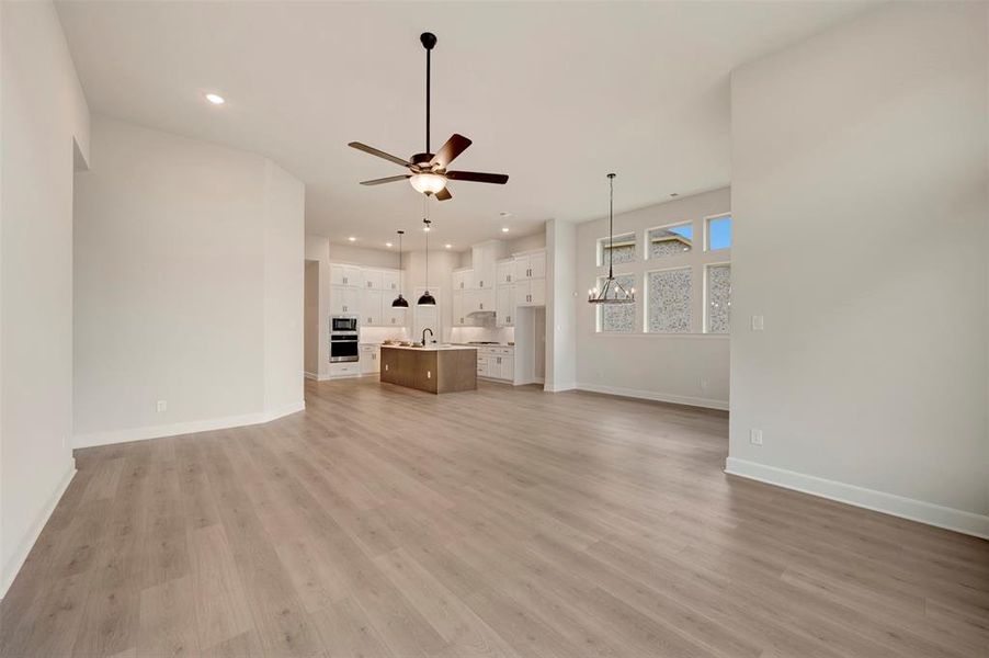Unfurnished living room featuring a chandelier, ceiling fan, and light wood-type flooring