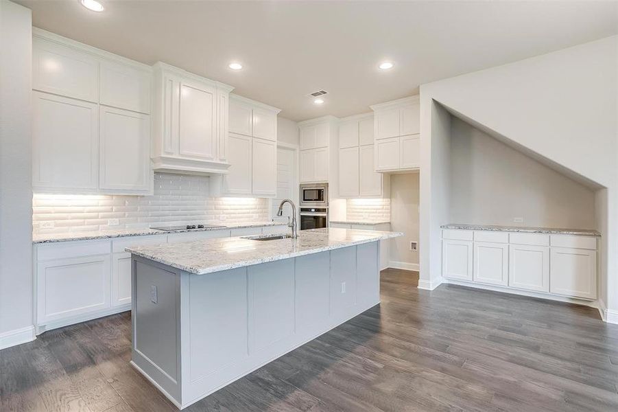 Kitchen featuring backsplash, an island with sink, dark hardwood / wood-style floors, appliances with stainless steel finishes, and sink