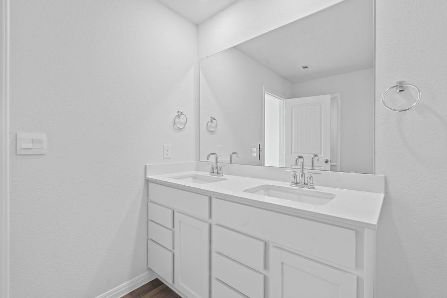 Bathroom featuring a textured wall, double vanity, and dark wood-style flooring Bathroom featuring a textured wall, double vanity, and dark wood-style flooring