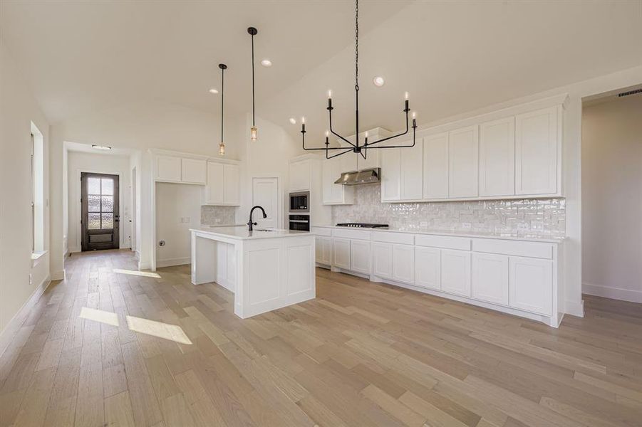 Kitchen with decorative backsplash, white cabinetry, light wood-style floors, a chandelier, and decorative light fixtures Kitchen with decorative backsplash, white cabinetry, light wood-style floors, a chandelier, and decorative light fixtures