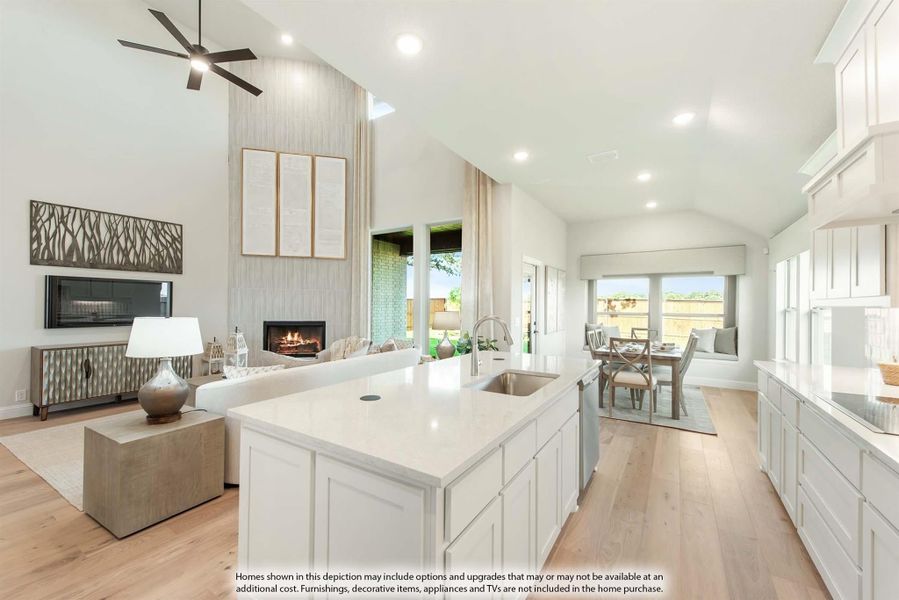 Open-concept kitchen with white island and cabinets flowing into living room with vaulted ceiling and fireplace