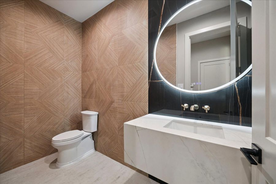 This elegant half bathroom features textured tile walls that create a sophisticated backdrop. A floating sink is paired with a modern lighted mirror, combining sleek design with functionality for a striking contemporary look.