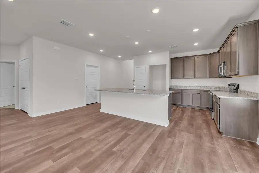 Kitchen with light stone countertops, recessed lighting, an island with sink, stainless steel appliances, and light wood-type flooring Kitchen with light stone countertops, recessed lighting, an island with sink, stainless steel appliances, and light wood-type flooring