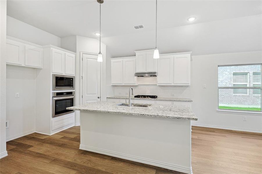 Kitchen with white cabinets, hanging light fixtures, sink, stainless steel appliances, and light hardwood / wood-style floors