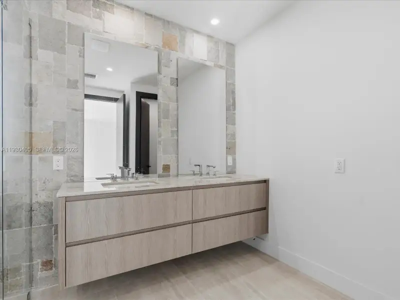 Floating vanity with wood-finish cabinetry, dual undermount sinks, stone-finish countertops, and natural stone tile backsplash with integrated vanity mirrors Floating vanity with wood-finish cabinetry, dual undermount sinks, stone-finish countertops, and natural stone tile backsplash with integrated vanity mirrors