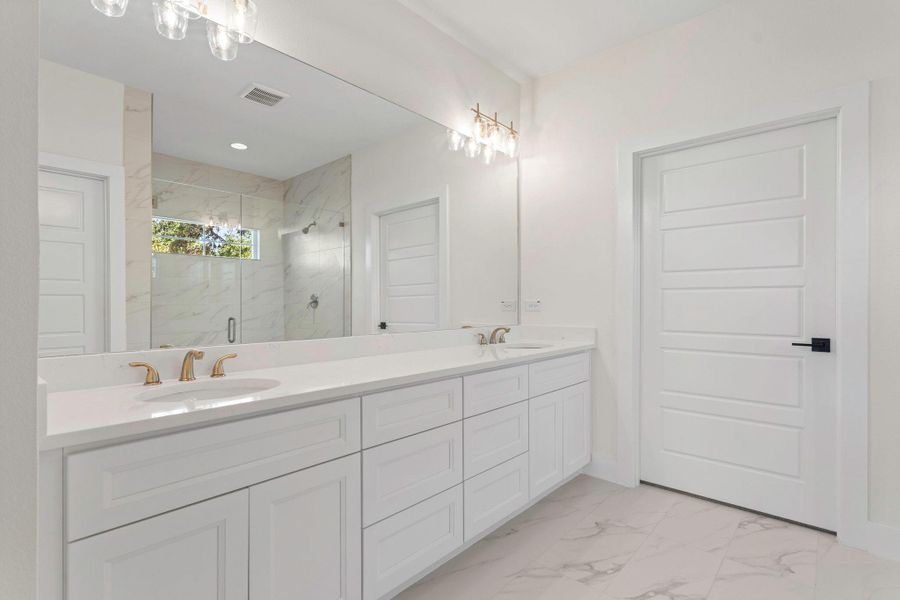 Double vanity featuring white cabinetry, light-toned countertops, and brass-finish hardware Double vanity featuring white cabinetry, light-toned countertops, and brass-finish hardware