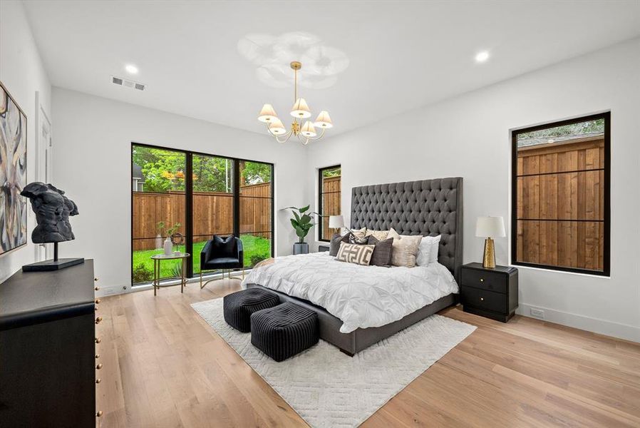 This room features light-toned hardwood flooring, a chandelier, and large windows
