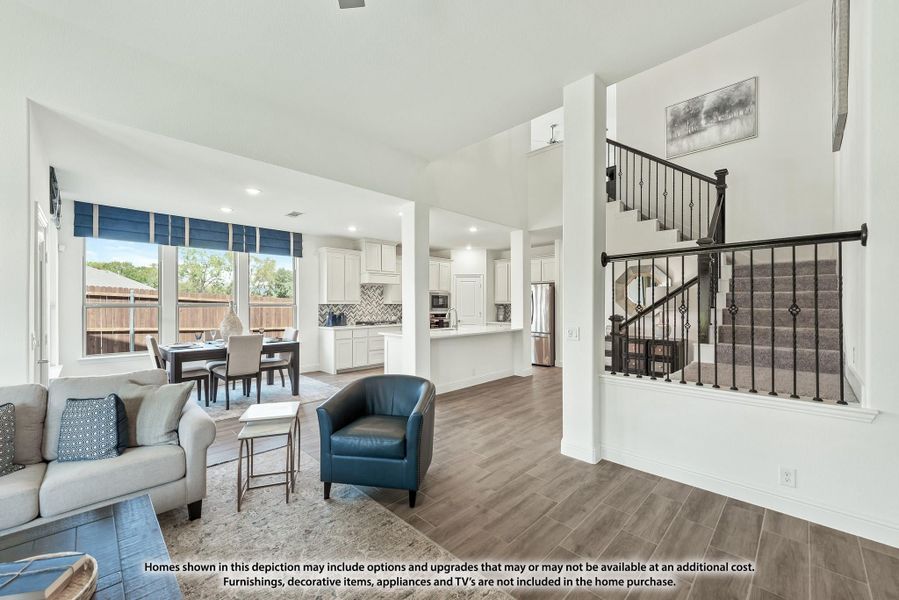 Open-concept living room with hardwood floors, staircase, and kitchen visible in background Open-concept living room with hardwood floors, staircase, and kitchen visible in background