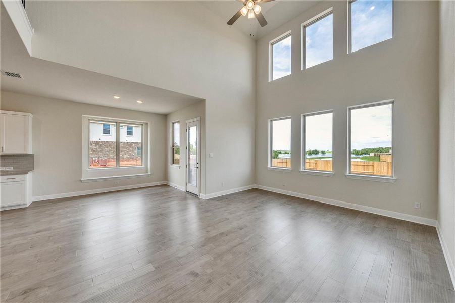 Unfurnished living room featuring plenty of natural light, ceiling fan, light wood-style flooring, and a towering ceiling Unfurnished living room featuring plenty of natural light, ceiling fan, light wood-style flooring, and a towering ceiling