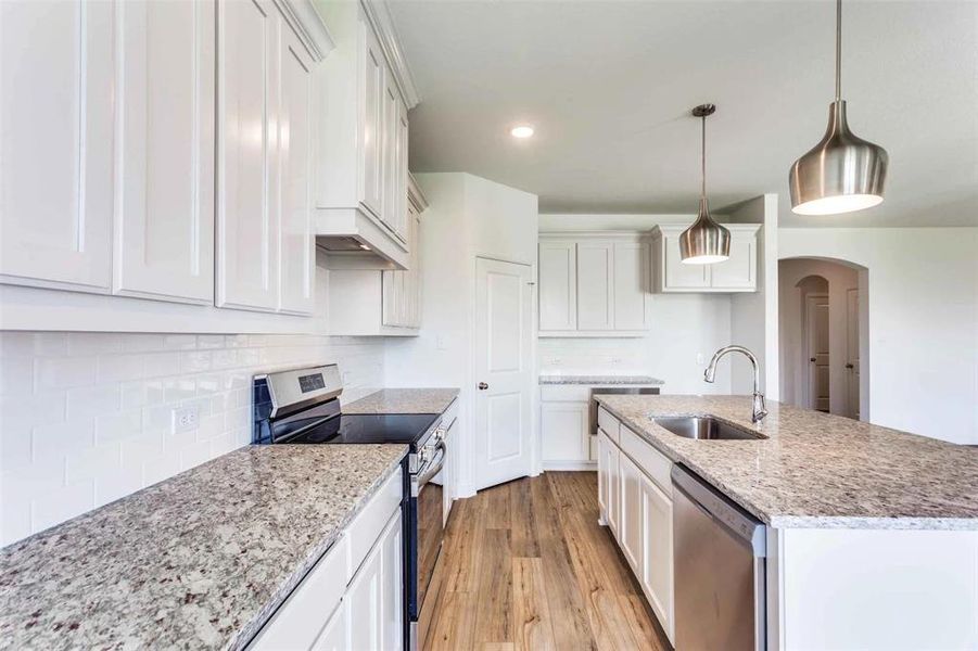 Kitchen featuring hanging light fixtures, sink, white cabinetry, appliances with stainless steel finishes, and light hardwood / wood-style floors