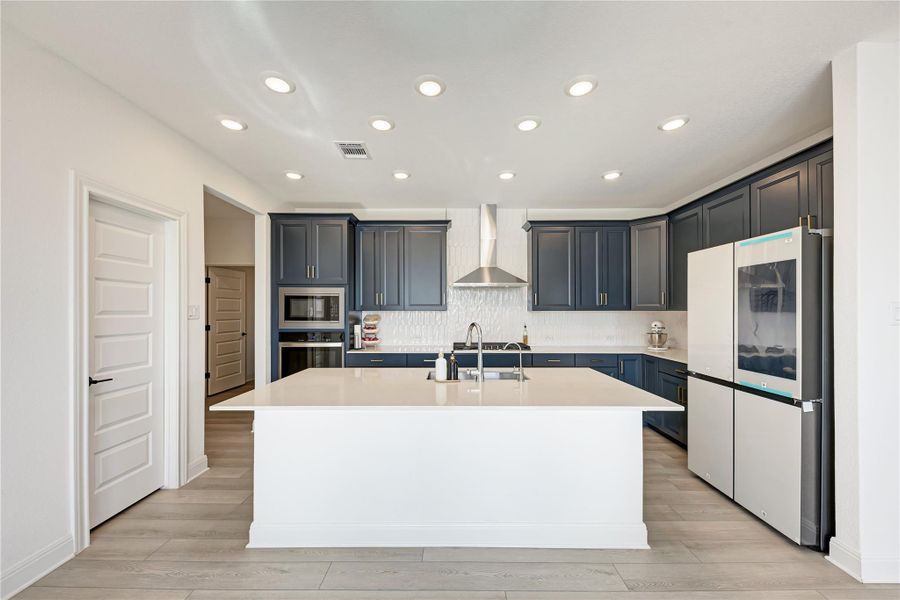 Modern kitchen featuring a central island with a sink, white quartz countertops, dark blue cabinetry, and wood-finish flooring