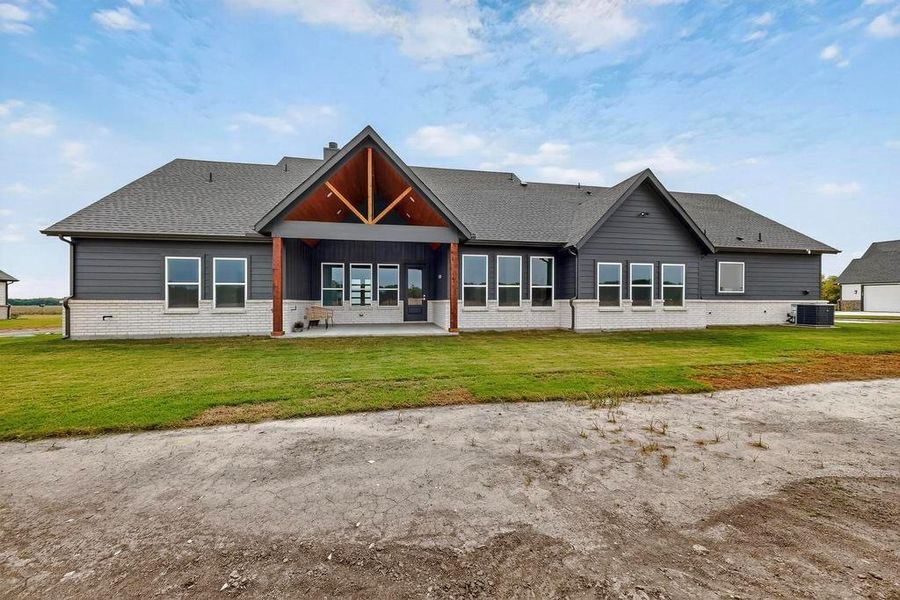 Back of property with a patio, a lawn, roof with shingles, and brick siding